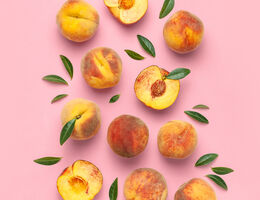 Whole and halved peaches and leaves on a pink background.