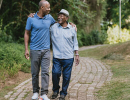 A younger man walks arm-in-arm with an older man.