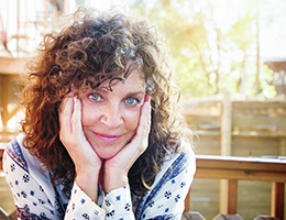 A smiling woman sits with her hands cupping her face.